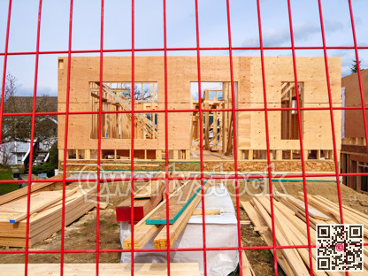 Wooden frame and walls of new house behind the red fence grid