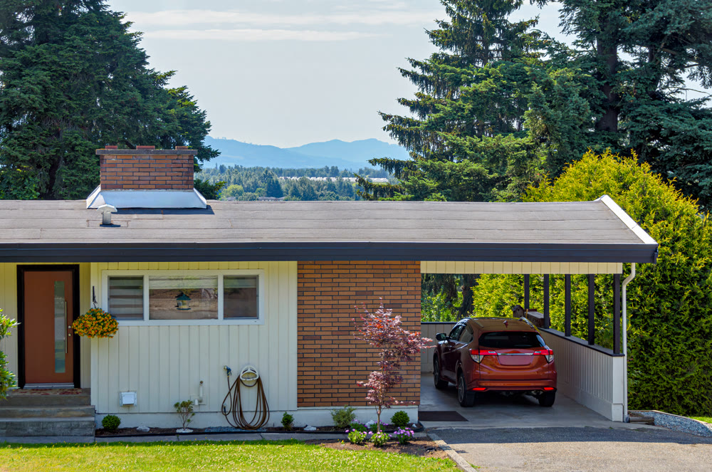 Average family house with mountain view and red car parked under the carport