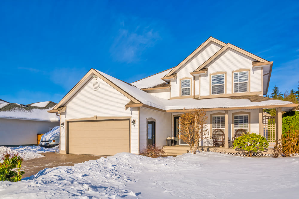 Family house with driveway and front yard in snow on winter sunny day
