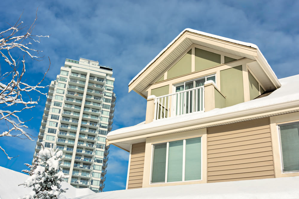 Top of residential house in snow and high-rise building on cloudy sky background