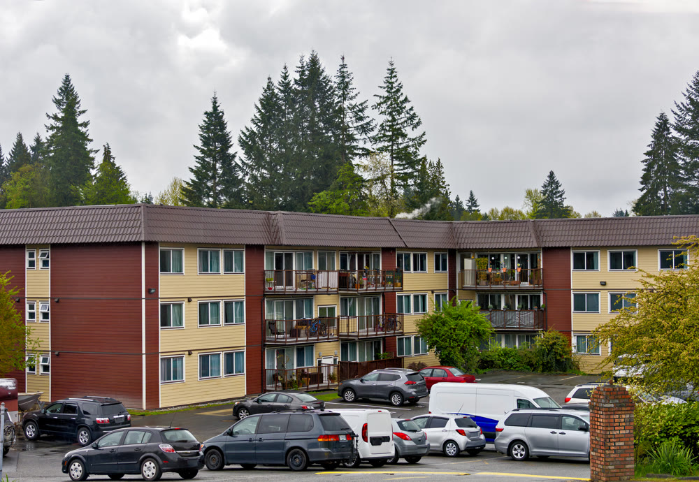Low-rise residential building with cars parked in front on overcast rainy day