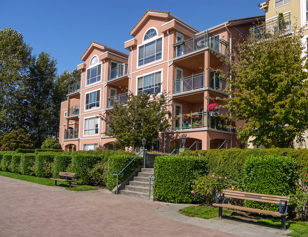 Apartement building on sunny day with bench and paved walkway in front
