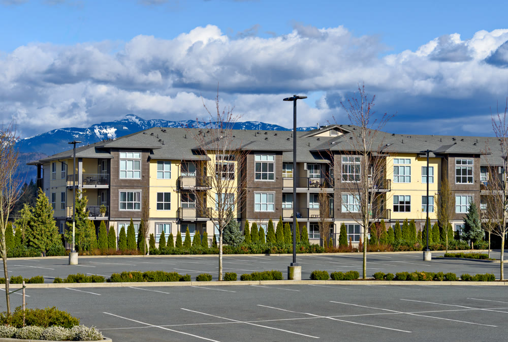 Low rise residential building with big parking lot in front on mountain background