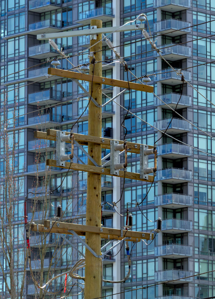 Power line wires mounted on wooden pole with high-rise building on the background