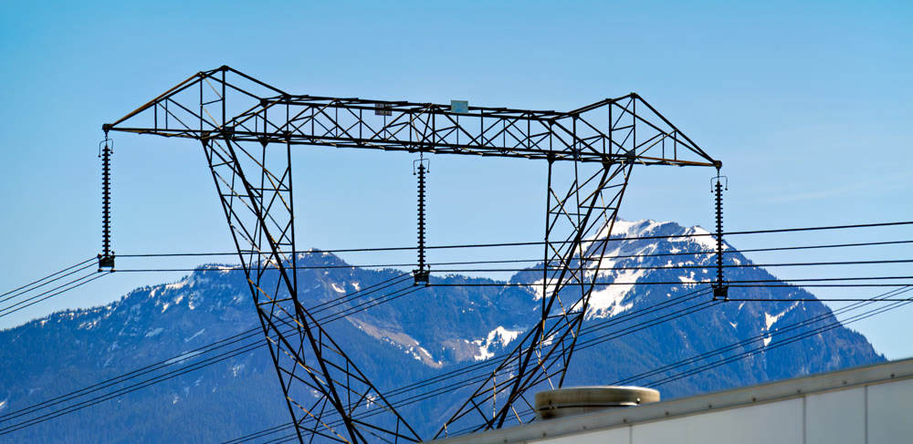 High voltage power lines and tower against snowy mountains