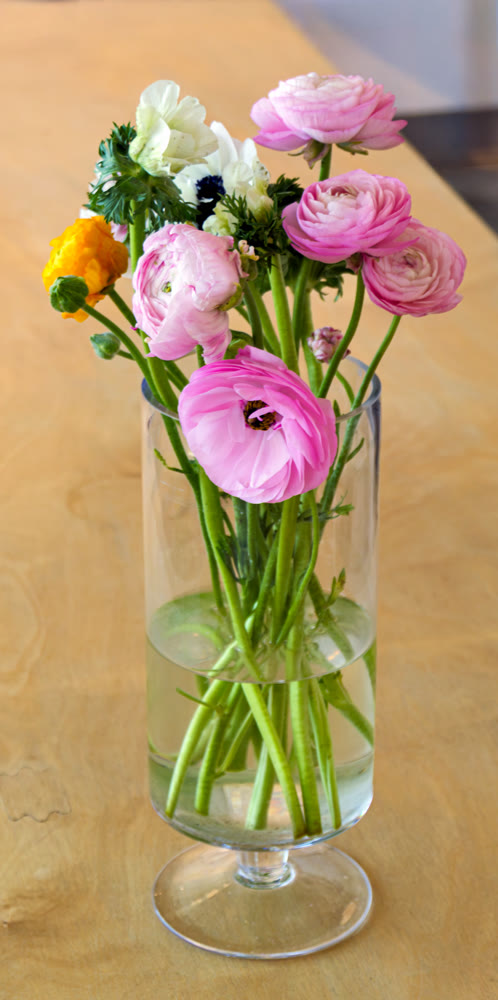 Pink ranunculus and anemone bouquet in a glass vase on a wooden table