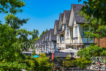 Perspective look at row of new townhouses surrounded by tree's leaves.
