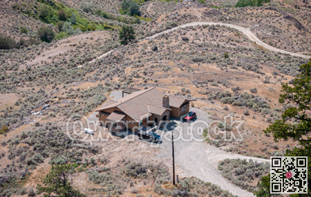Rancho house with cars parked beside in the middle of desert with gravel road