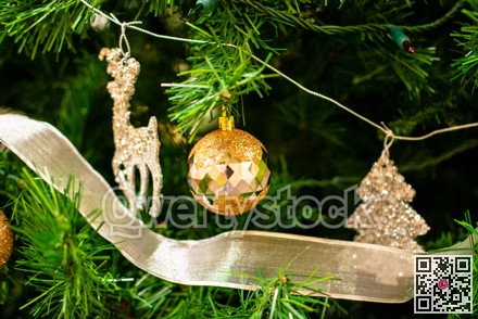 Golden bauble among chistmas tree brenches. Closeup look of the ball.