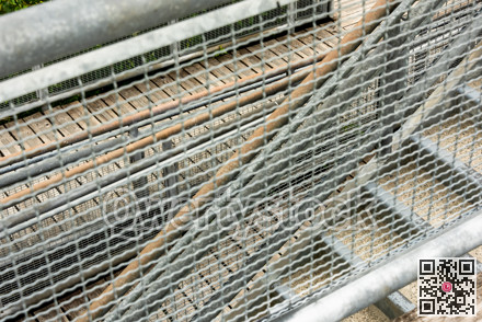 Abstract look through the metal grid on stairs and wooden deck in a park