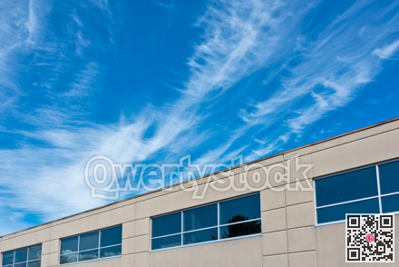 Top of the office building with windows on blue and cloudy sky background