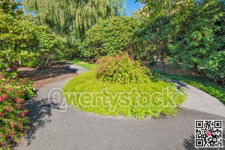 Paved pathway through a park with round flowerbed in the middle