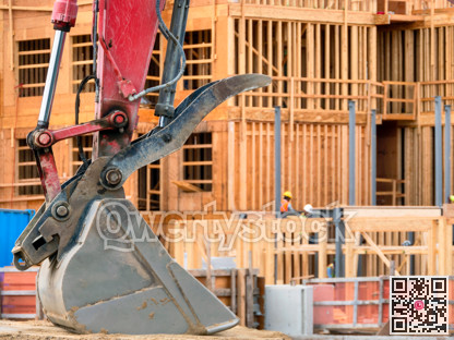 Metal excavator bucket on low-rise building construction background
